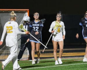 High school lacrosse players in action on a night field, showcasing teamwork and competitive spirit during a game.