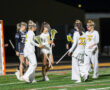 Girls' lacrosse players celebrate on the field during a night game, showcasing teamwork and athletic spirit.