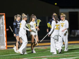 Girls' lacrosse players celebrate on the field during a night game, showcasing teamwork and athletic spirit.