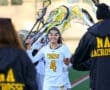 A lacrosse player in a white jersey high-fives teammates on the field, showcasing team spirit and sportsmanship.