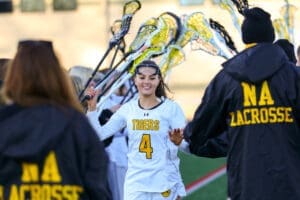 A lacrosse player in a white jersey high-fives teammates on the field, showcasing team spirit and sportsmanship.