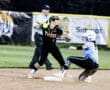 Softball player in black catches a ball to tag a sliding runner in blue. Umpire watches closely during intense game action.