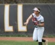 Young female softball player preparing to throw, wearing a jersey and cap, with a focused expression in an outdoor field setting.