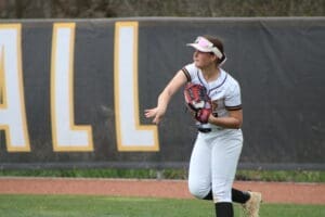 Young female softball player preparing to throw, wearing a jersey and cap, with a focused expression in an outdoor field setting.
