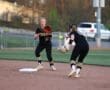 Two softball players in black uniforms catch and throw a ball during practice on a well-maintained field.