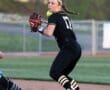 Female softball player in black uniform catches a ball while a player slides into base, showcasing athletic action.