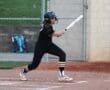 A young female softball player swings a bat at home plate during a game, focused and ready to hit.