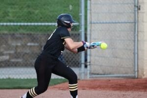 Young female softball player prepares to bunt as the pitch approaches during a game on the field.