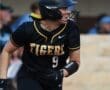 Softball player in a black Tigers uniform, number 9, running on the field during a game. Focused and determined expression.