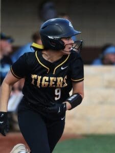Softball player in a black Tigers uniform, number 9, running on the field during a game. Focused and determined expression.