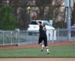 A softball player leaps to catch a fly ball during an outdoor game, showcasing athleticism and determination.