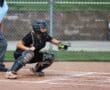 Young female softball catcher in action, preparing to catch a pitch during a game, with umpire in the background.