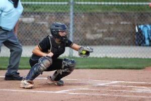Young female softball catcher in action, preparing to catch a pitch during a game, with umpire in the background.