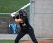 Player in a black softball uniform prepares to bat, showcasing focus and determination on the field.
