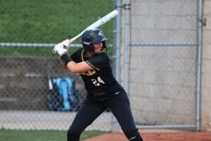Player in a black softball uniform prepares to bat, showcasing focus and determination on the field.
