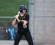 Young female softball player at bat, wearing a black uniform with yellow accents, ready for the pitch on a diamond.