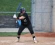 Young female softball player in a black uniform prepares to bat on a field, showcasing athleticism and focus.