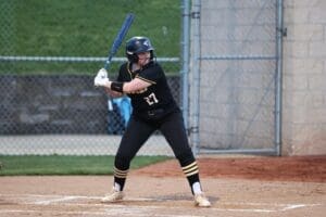 Young female softball player in a black uniform prepares to bat on a field, showcasing athleticism and focus.