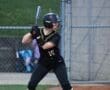 A young female softball player in a black jersey and helmet prepares to bat at a game.