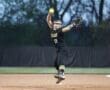 A female softball pitcher in action, wearing a black uniform and preparing to throw a bright yellow ball.