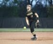 Softball player in uniform throwing a pitch during a game, showcasing athleticism on the field at dusk.