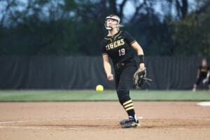 Softball player in uniform throwing a pitch during a game, showcasing athleticism on the field at dusk.