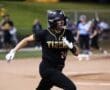A female softball player in a black uniform runs the bases during a game, showcasing athleticism and team spirit.