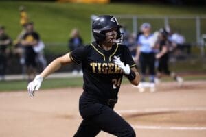 A female softball player in a black uniform runs the bases during a game, showcasing athleticism and team spirit.