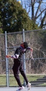 A young tennis player serves the ball on a sunny court, showcasing focus and athleticism during practice.