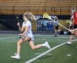 High school girls' lacrosse player sprinting on field, stick in hand, during an evening match. Excitement in the air!