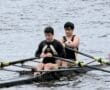 Two rowers in a double scull boat, focused on their technique while navigating a calm waterway.