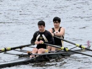 Two rowers in a double scull boat, focused on their technique while navigating a calm waterway.