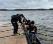 Team of young rowers preparing on the dock, receiving guidance before heading out on the water on an overcast day.