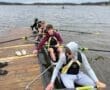 Rowers preparing their boat on a cloudy day at the lake, focusing on teamwork and technique before practice.