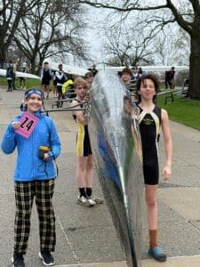 Rowing team members pose with a sleek boat before a competition, showcasing excitement and team spirit.