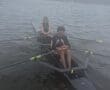 Two rowers in a boat on a lake, preparing for practice on a cloudy day, showcasing teamwork and athleticism.