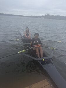 Two rowers in a boat on a lake, preparing for practice on a cloudy day, showcasing teamwork and athleticism.