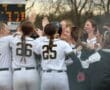 Girls’ softball team celebrating a play, showcasing teamwork and excitement with smiles and high fives.