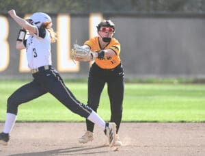 Softball players in action; one attempts to steal second base as the fielder prepares to make the catch.