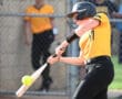 A softball player swings at a yellow ball during a game, capturing an action shot of the sport.
