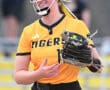 Softball player wearing a yellow Tigers jersey smiles while holding her glove during a game. Team spirit on display!
