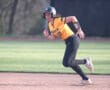 Female softball player in a black and yellow uniform running on the field during a game, showcasing athleticism and focus.