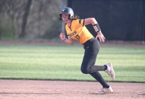 Female softball player in a black and yellow uniform running on the field during a game, showcasing athleticism and focus.