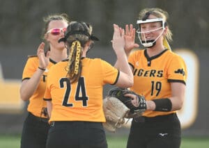 Softball players in yellow jerseys celebrating during a game, showcasing teamwork and excitement on the field.
