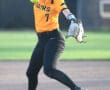 A young female softball player in an orange jersey throws a pitch on a sunny field, showcasing athletic form and focus.