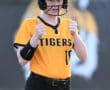 Young softball player in a Tigers uniform gives two thumbs up, celebrating a successful play during a game.