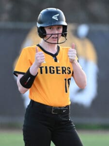 Young softball player in a Tigers uniform gives two thumbs up, celebrating a successful play during a game.