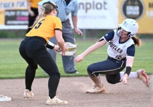 Two softball players compete for the base during a game, showcasing athleticism on a dirt field under bright lights.