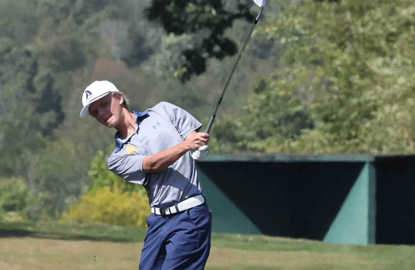 Young golfer in action, swinging a club on a sunny course, surrounded by trees and vibrant greenery.