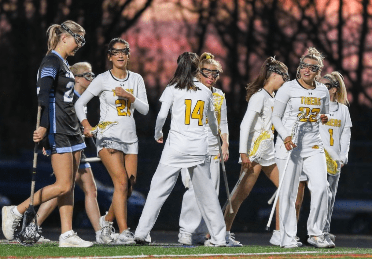 High school girls' lacrosse team celebrating on the field during an evening game, showcasing team spirit and camaraderie.